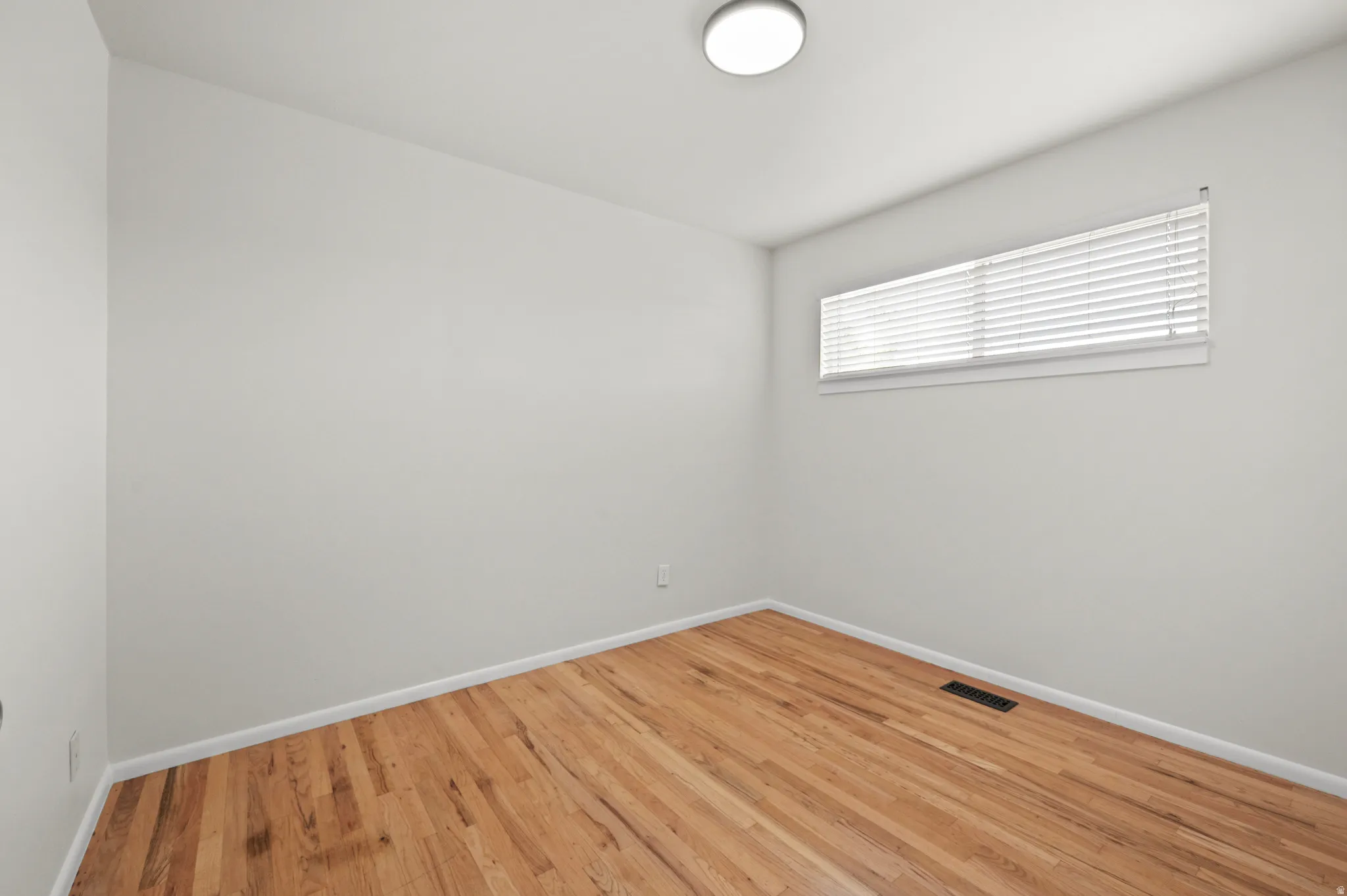 Hardwood flooring, white walls, and a horizontal window with blinds