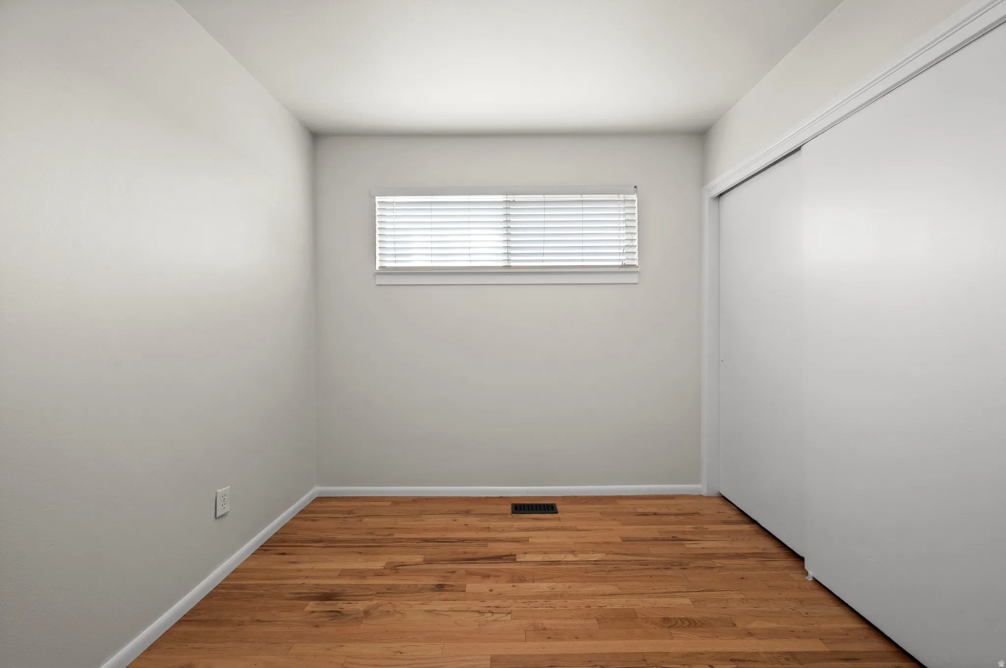 Wood-finish flooring, white walls, window with blinds, and white bi-fold closet doors