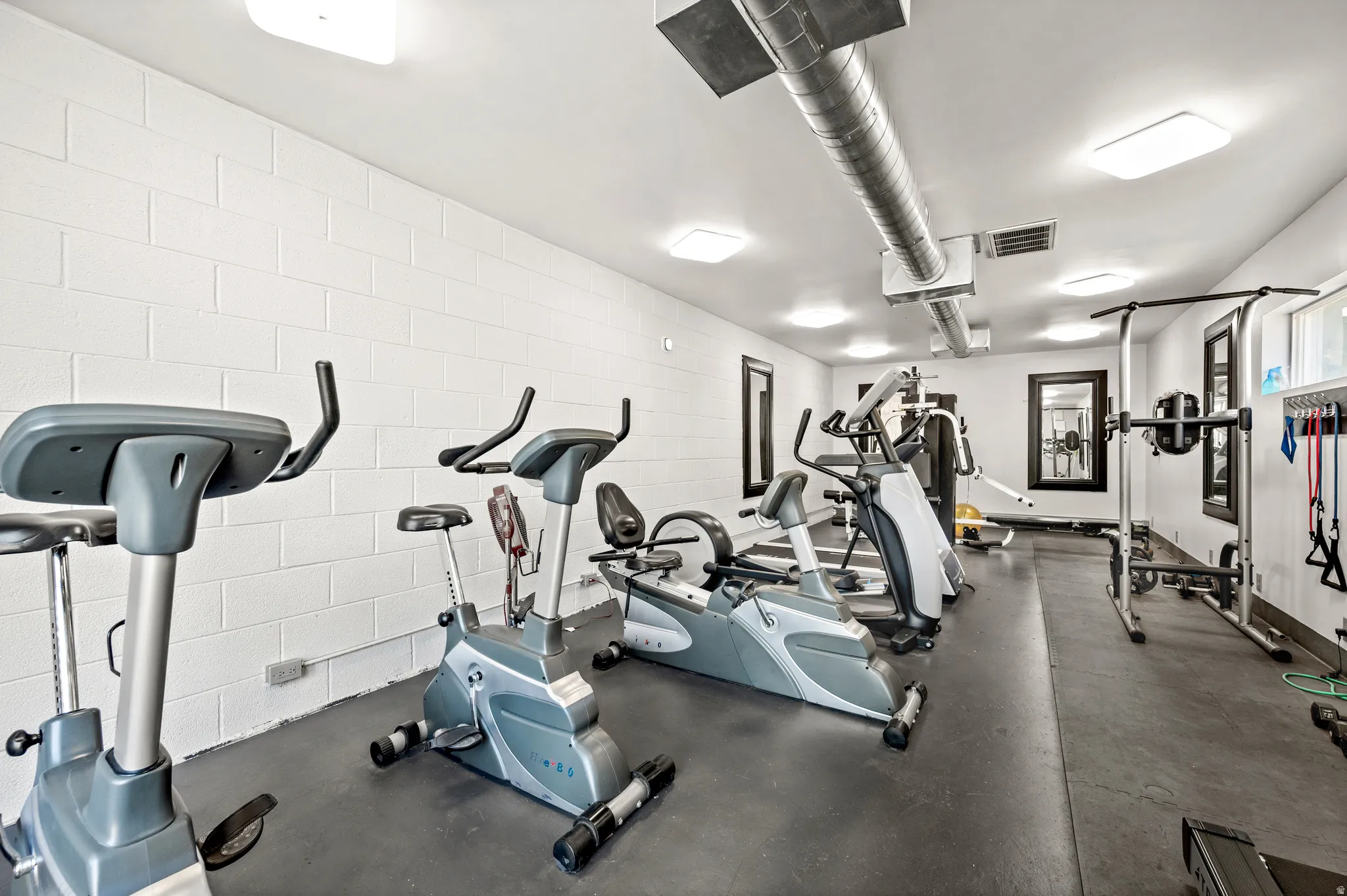Dedicated fitness area with white block walls, exposed ductwork, and recessed lighting