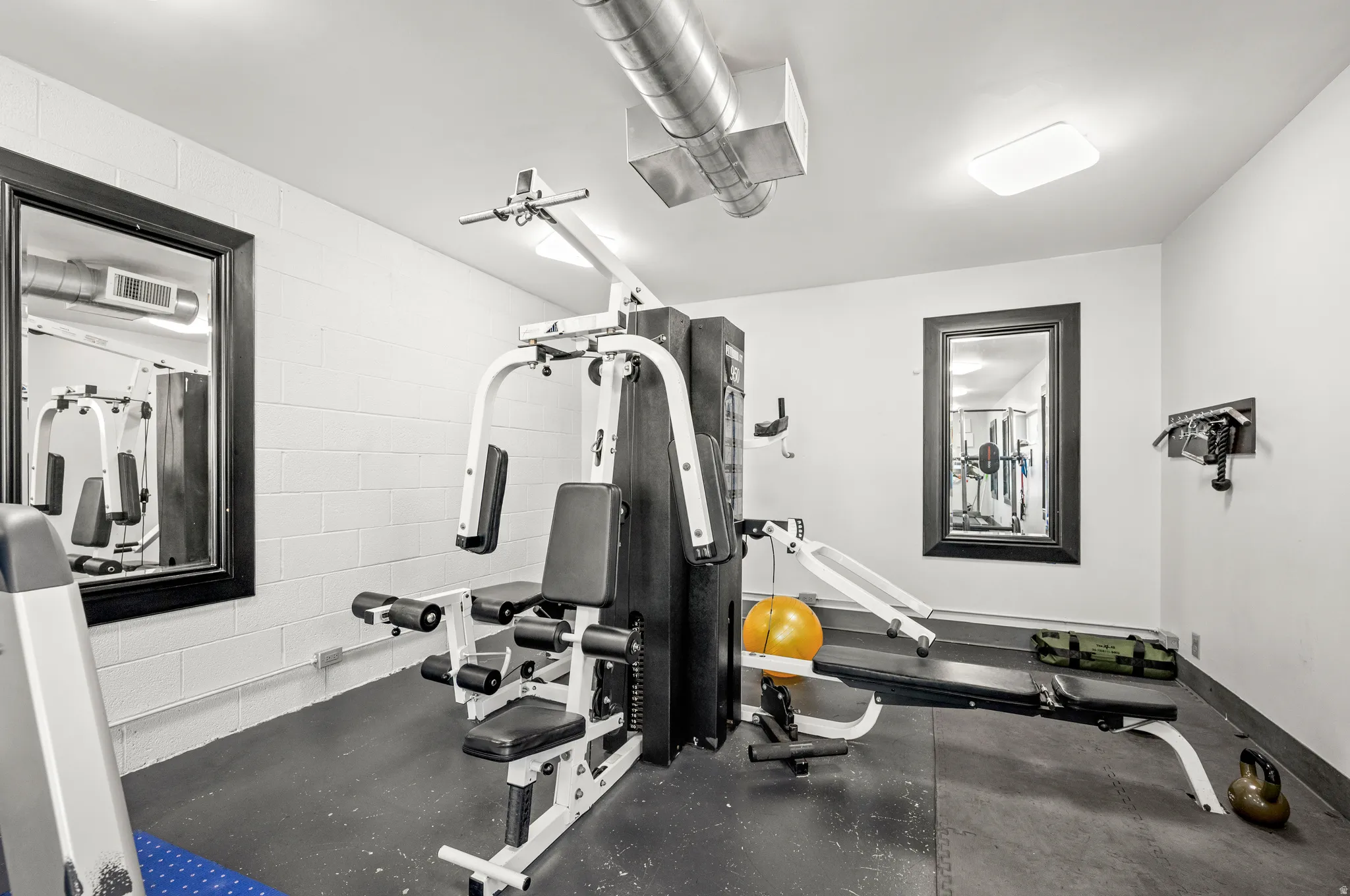 Dedicated fitness area featuring white block walls, dark flooring, and exposed ductwork