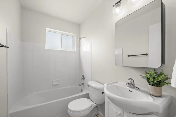 White ceramic tile tub surround with window, wall-mounted vanity with integrated sink, chrome faucet, and rectangular framed mirror
