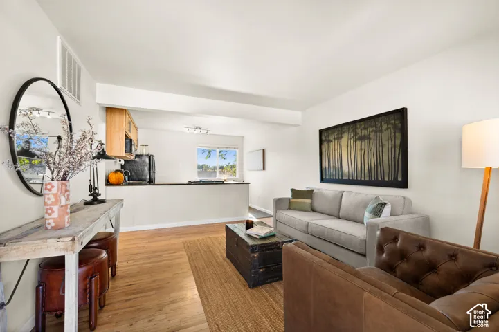 Open-concept interior featuring light wood-finish flooring, a pass-through kitchen peninsula, and a horizontal window providing natural light