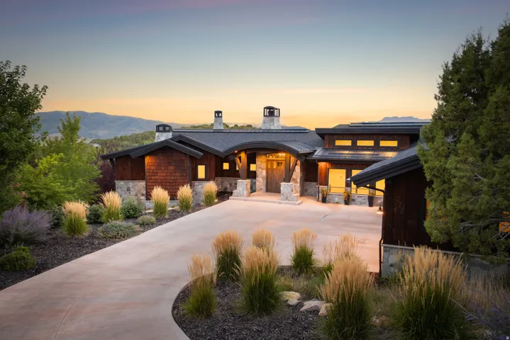 Contemporary residence featuring a curved roofline, stone and wood shingle exterior, multiple prominent chimneys, and an expansive concrete driveway