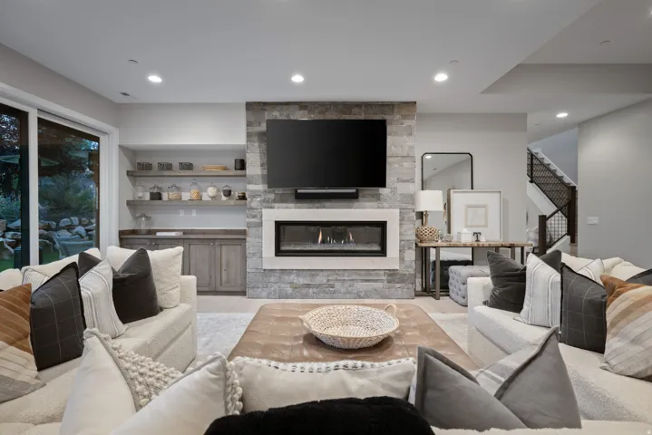 Stone-clad fireplace with a linear insert, built-in shelving, glass sliding doors, recessed lighting, and a staircase with metal balusters