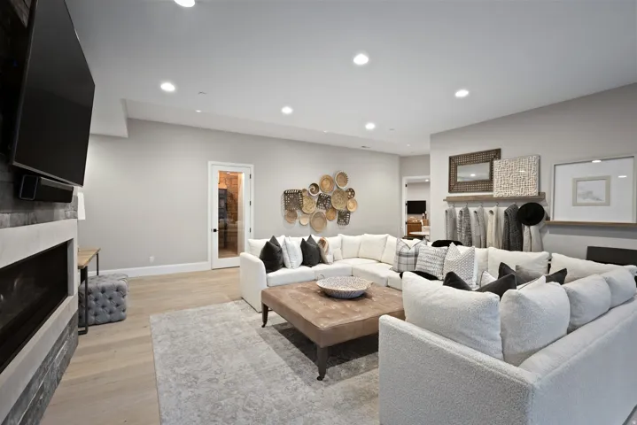 Recessed lighting throughout, stone-clad fireplace, light wood-finish flooring, and white interior doors with black hardware