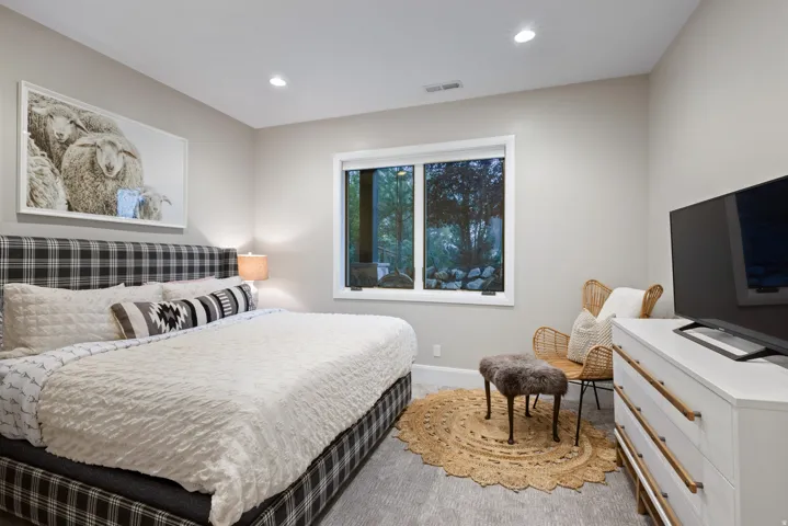 Recessed lighting illuminates the room, featuring light gray walls, light gray wood-finish flooring, and a window with white trim