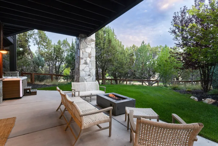 Covered patio featuring a stone-clad pillar, built-in hot tub, concrete fire pit, and a grass lawn