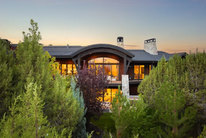 Stone and wood-clad exterior with a dark shingle roof, featuring multiple balconies, large arched windows, and a prominent stone chimney