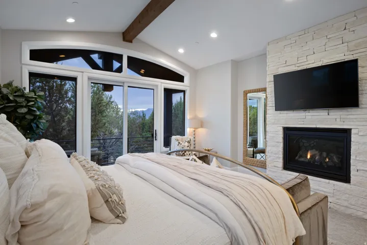 Vaulted ceiling with an exposed wood beam, recessed lighting, a built-in fireplace with a stone surround, and floor-to-ceiling windows with an arched transom