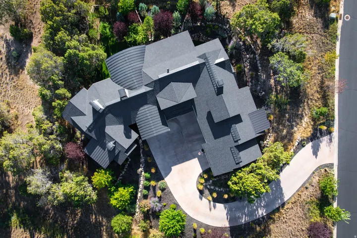 Asphalt shingle roof with varied pitches, concrete driveway, stone retaining walls, and mature landscaping