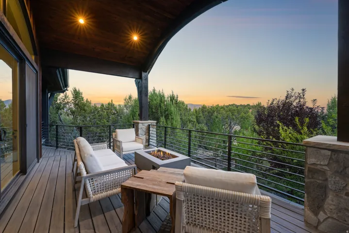 Expansive outdoor deck with wood-finish flooring, a built-in fire pit, stone-clad pillars, and a black metal railing