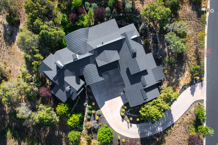 Expansive property featuring a multi-level roofline, extensive paved driveway, mature trees, and varied landscaping