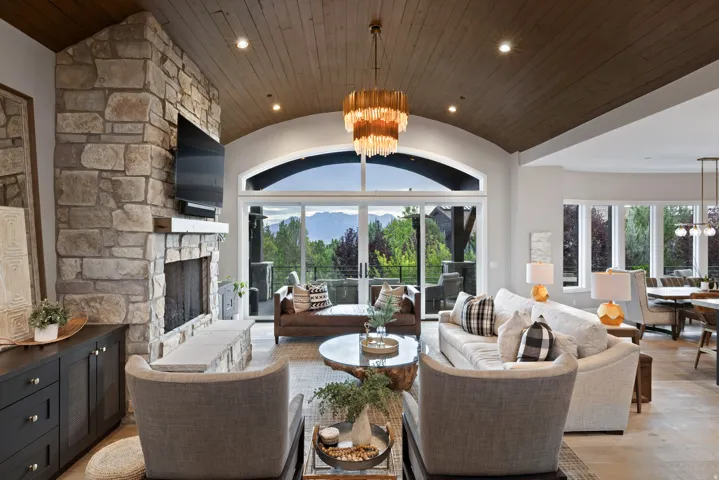Arched wood-paneled ceiling, stone-clad fireplace with mantel, sliding glass doors, recessed lighting, and a decorative chandelier