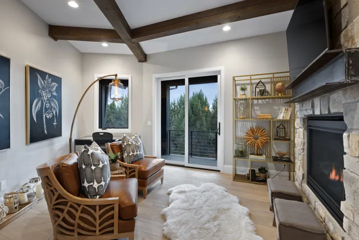 Exposed wood ceiling beams, stone fireplace, light wood-finish flooring, sliding glass door, and recessed lighting