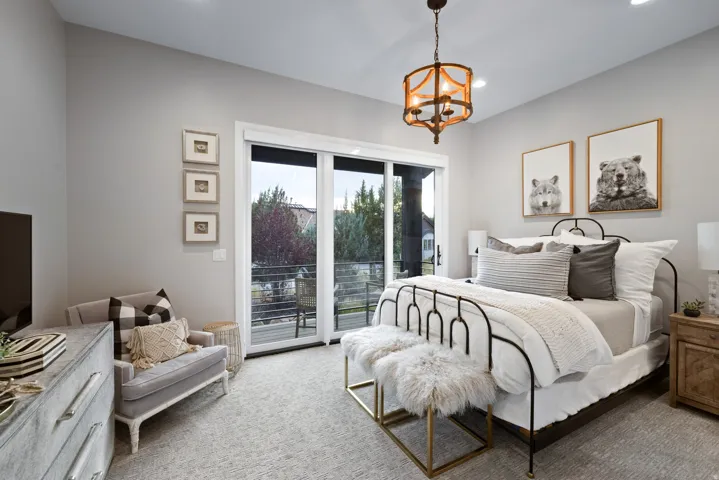 Sliding glass door leading to an outdoor balcony, overhead chandelier, light gray wall finish, and a black metal bed frame