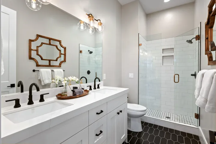 Dual vanity with white cabinetry and integrated sinks, matte black plumbing fixtures, glass-enclosed shower with subway tile, and dark hexagonal floor tiling