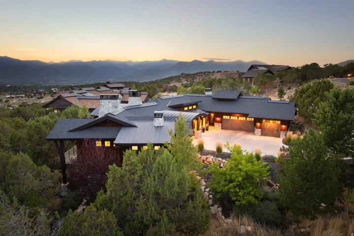 Expansive mountain backdrop, dark-pitched roofing, integrated garage spaces, stone chimney, and established landscaping