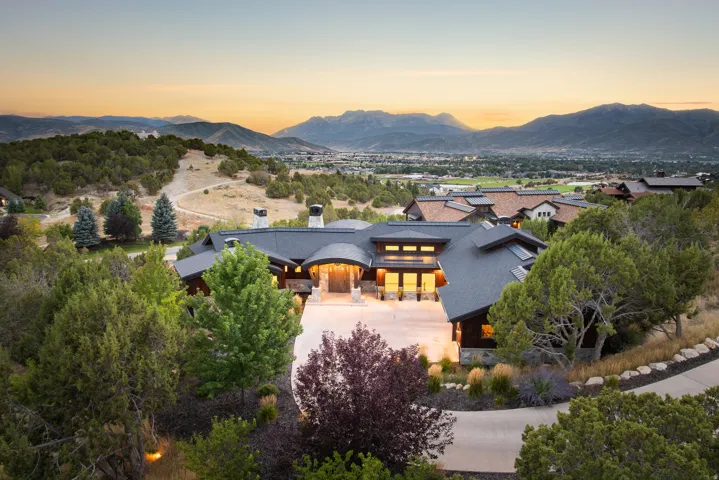 Mountain backdrop with expansive property featuring a paved driveway, mature trees, and a modern exterior with varied rooflines