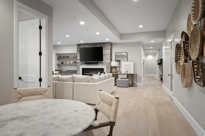 Spacious living area featuring light wood-finish flooring, recessed lighting, and a stone-clad fireplace with built-in shelving