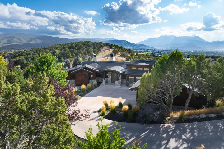 Expansive concrete driveway, stone and wood-clad exterior, tiered landscaping, and a mountainous backdrop