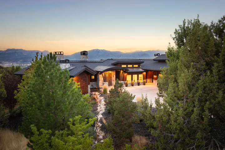 Contemporary architecture featuring a dark roof, stone and wood siding, multiple chimneys, and a prominent driveway