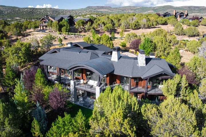 Multi-level architectural design featuring expansive balconies, stone columns, dark wood siding, and multiple chimneys