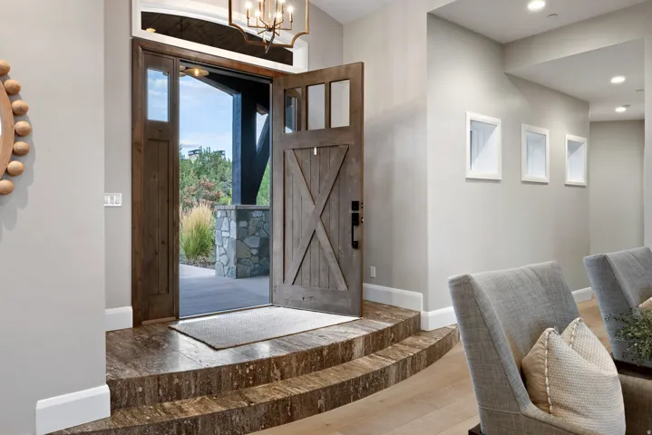 Double entry doors with transom window, stone steps, chandelier lighting, and recessed wall niches