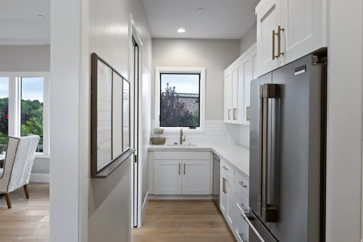 Galley kitchen with wood-finish flooring, white cabinetry, integrated stainless steel refrigerator, white subway tile backsplash, and a single window