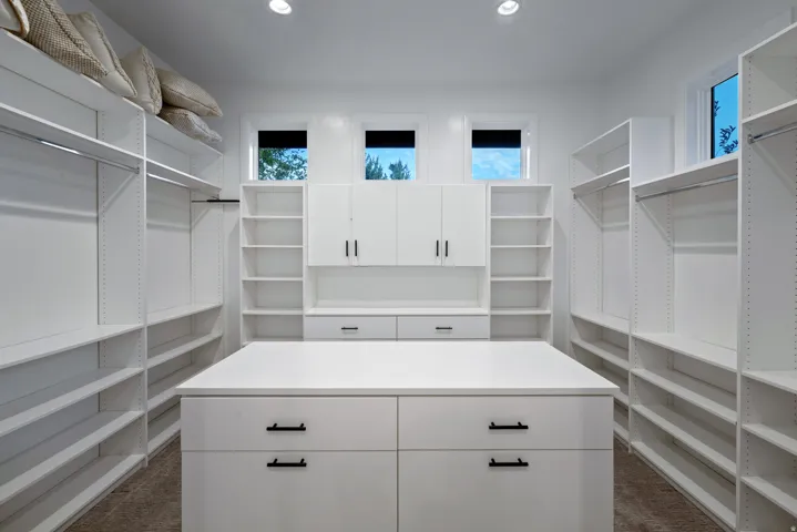 Expansive custom closet featuring an integrated center island with drawer storage, ample shelving, built-in cabinetry, and multiple windows for natural light