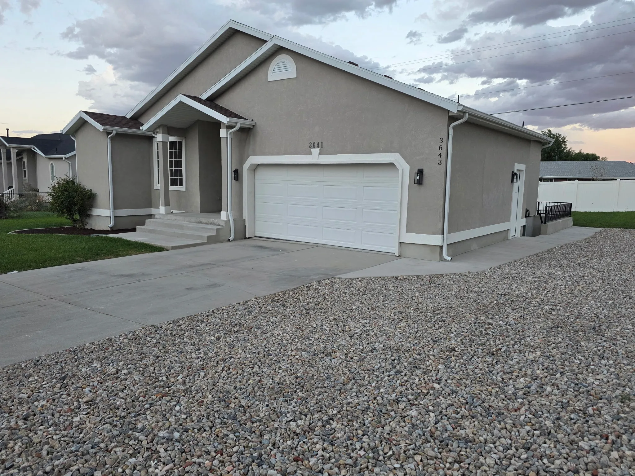 Stucco exterior with a two-car garage, concrete driveway, and gravel parking area