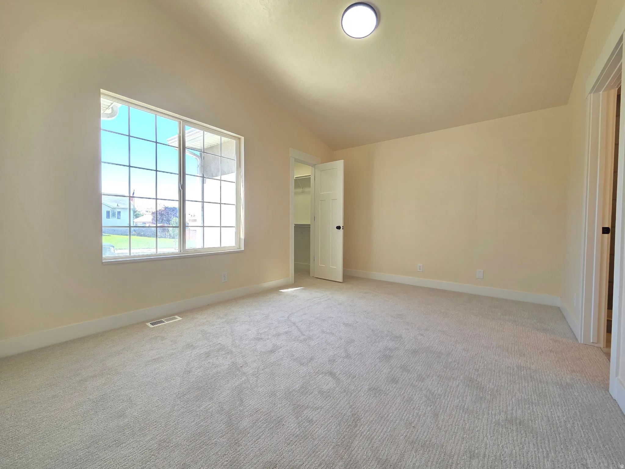 Neutral-toned carpeting, ample natural light from a grid-pattern window, neutral wall paint, and a flush-mount ceiling light