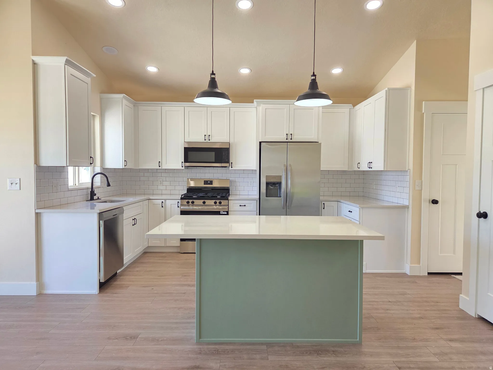 Kitchen featuring white shaker cabinetry, stainless steel appliances, light-toned wood-finish flooring, a subway tile backsplash, and a central island with a contrasting base
