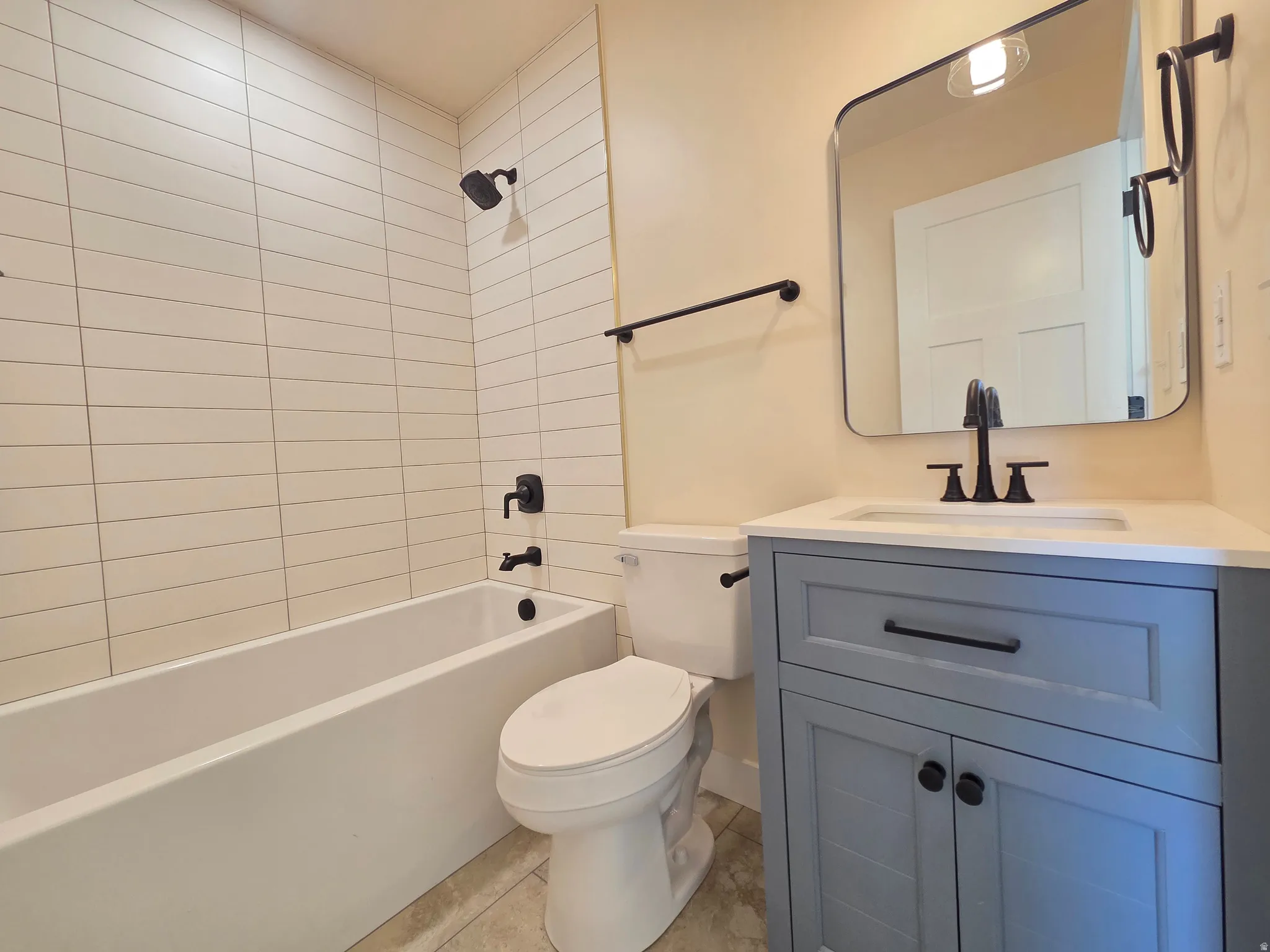 Bathroom featuring a white bathtub, subway tile shower surround, a light blue vanity with an integrated sink, and black fixtures