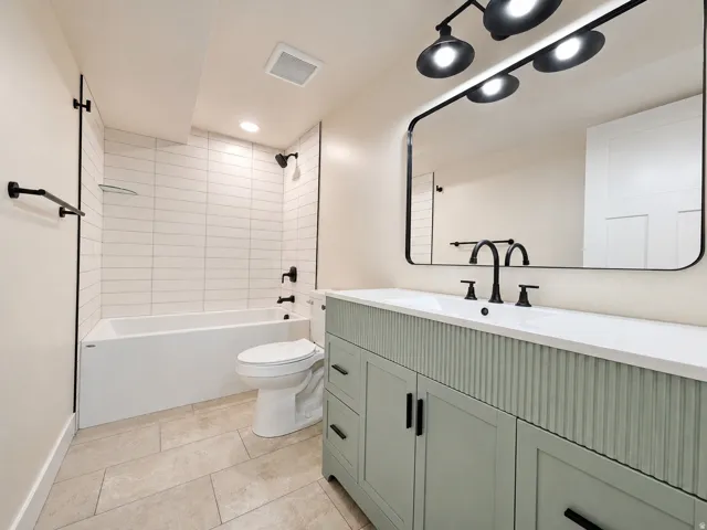Light-toned tile flooring, white subway tile shower surround, and a vanity with reeded paneling