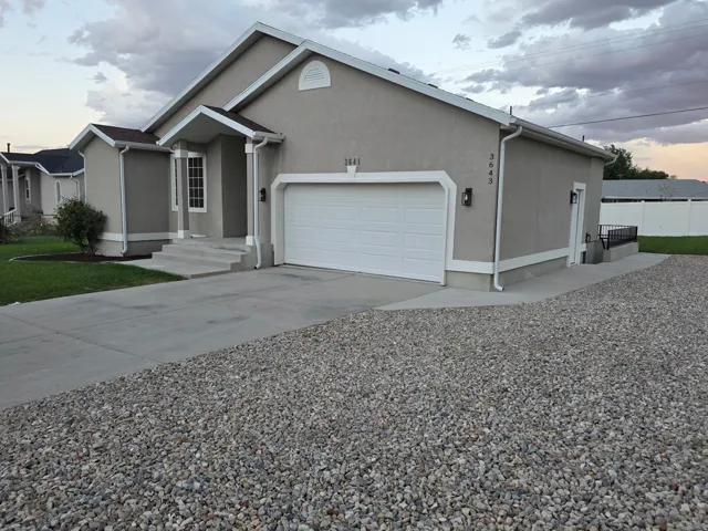Stucco exterior with a two-car garage, concrete driveway, and gravel parking area