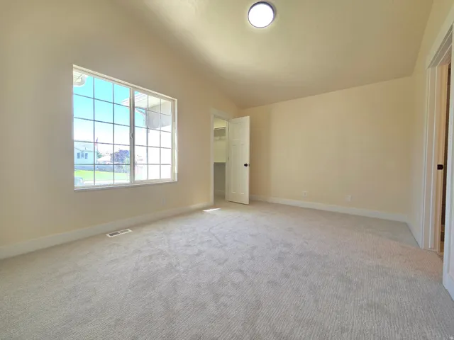 Neutral-toned carpeting, ample natural light from a grid-pattern window, neutral wall paint, and a flush-mount ceiling light