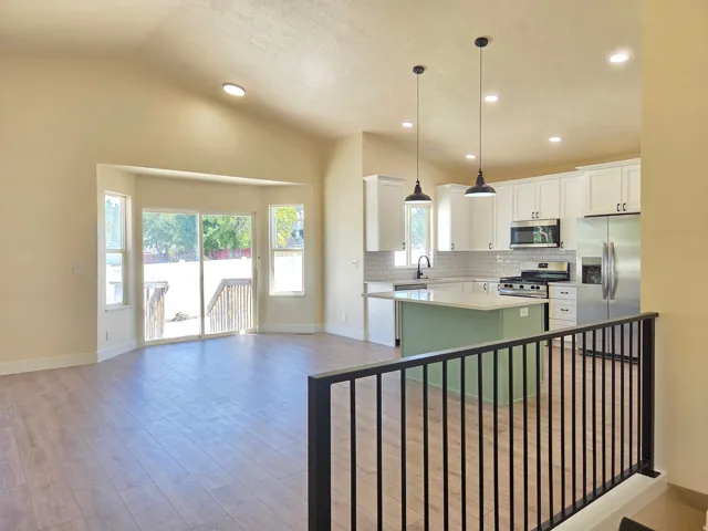 Vaulted ceilings complemented by recessed lighting, wood-finish flooring, a kitchen island with pendant lighting, a stainless steel appliance suite, and white cabinetry