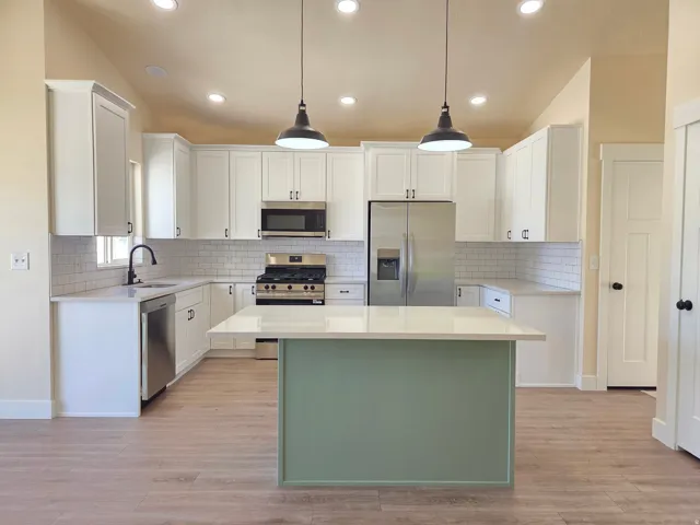 Kitchen featuring white shaker cabinetry, stainless steel appliances, light-toned wood-finish flooring, a subway tile backsplash, and a central island with a contrasting base