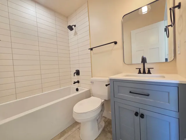 Bathroom featuring a white bathtub, subway tile shower surround, a light blue vanity with an integrated sink, and black fixtures