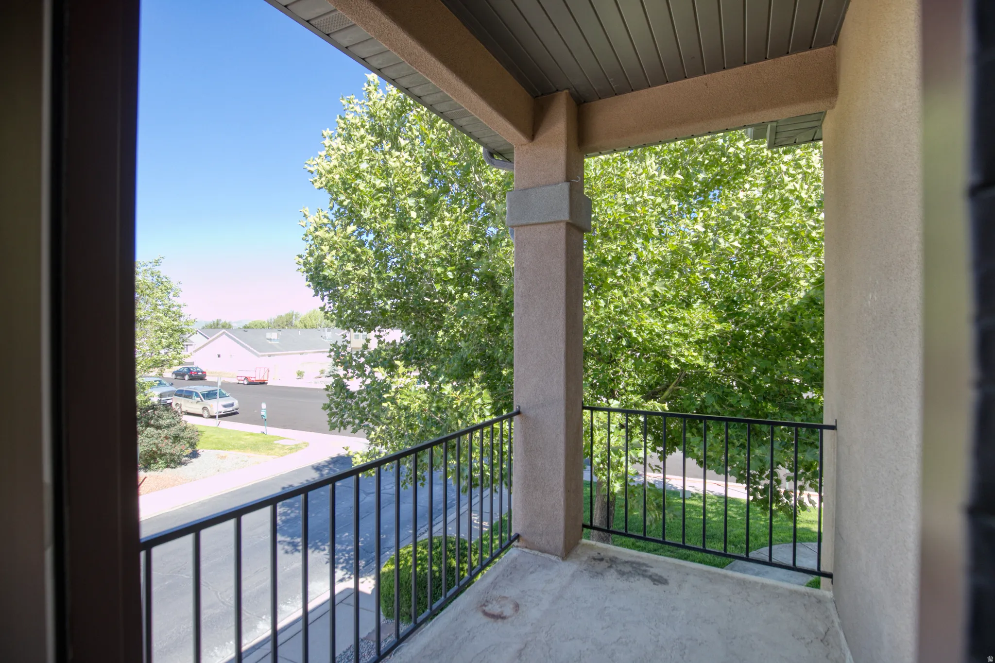 Private balcony with a stucco exterior, concrete flooring, and black metal railing
