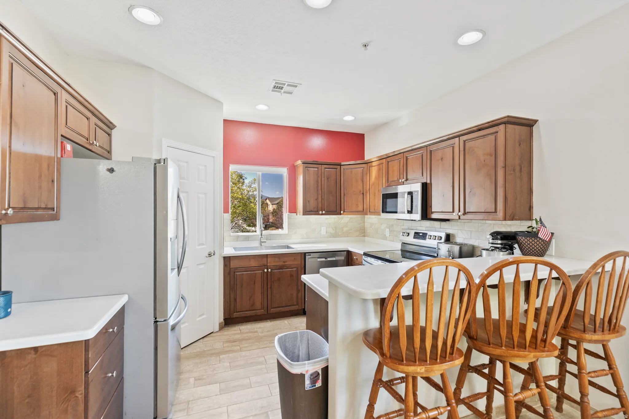 Stainless steel appliances, recessed lighting, wood-finish cabinetry, light-toned countertops, and tile flooring
