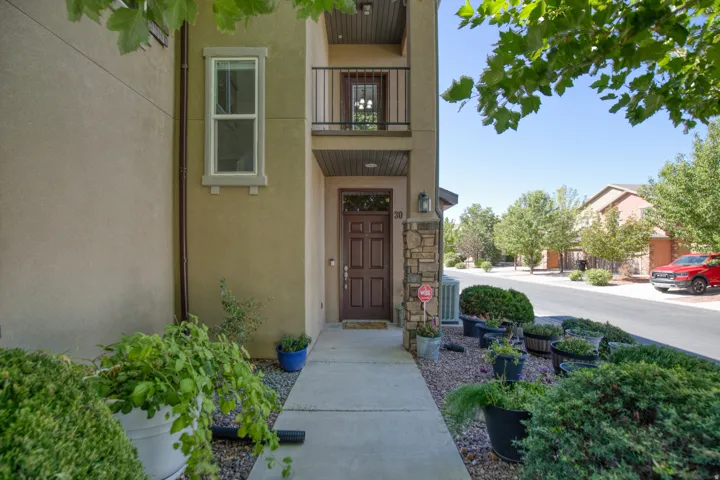 Stucco exterior with stone accent column, dark wood-finish entry door, and second-story balcony with iron railing