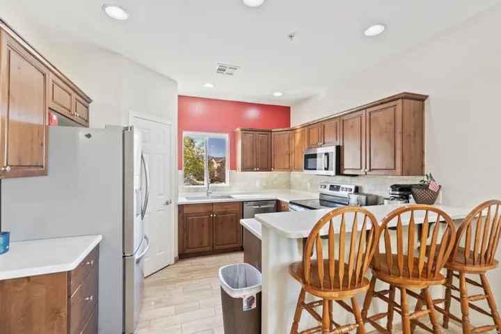 Stainless steel appliances, recessed lighting, wood-finish cabinetry, light-toned countertops, and tile flooring