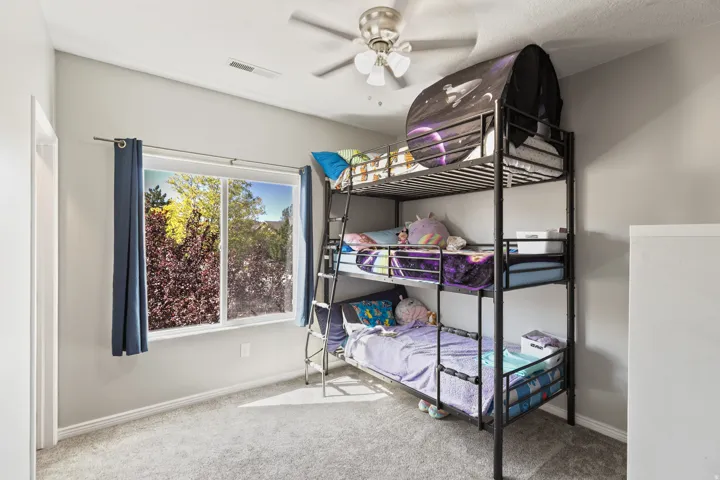 Room with light gray walls, a window featuring exterior landscaping, light gray carpet, and a ceiling fan with integrated lighting