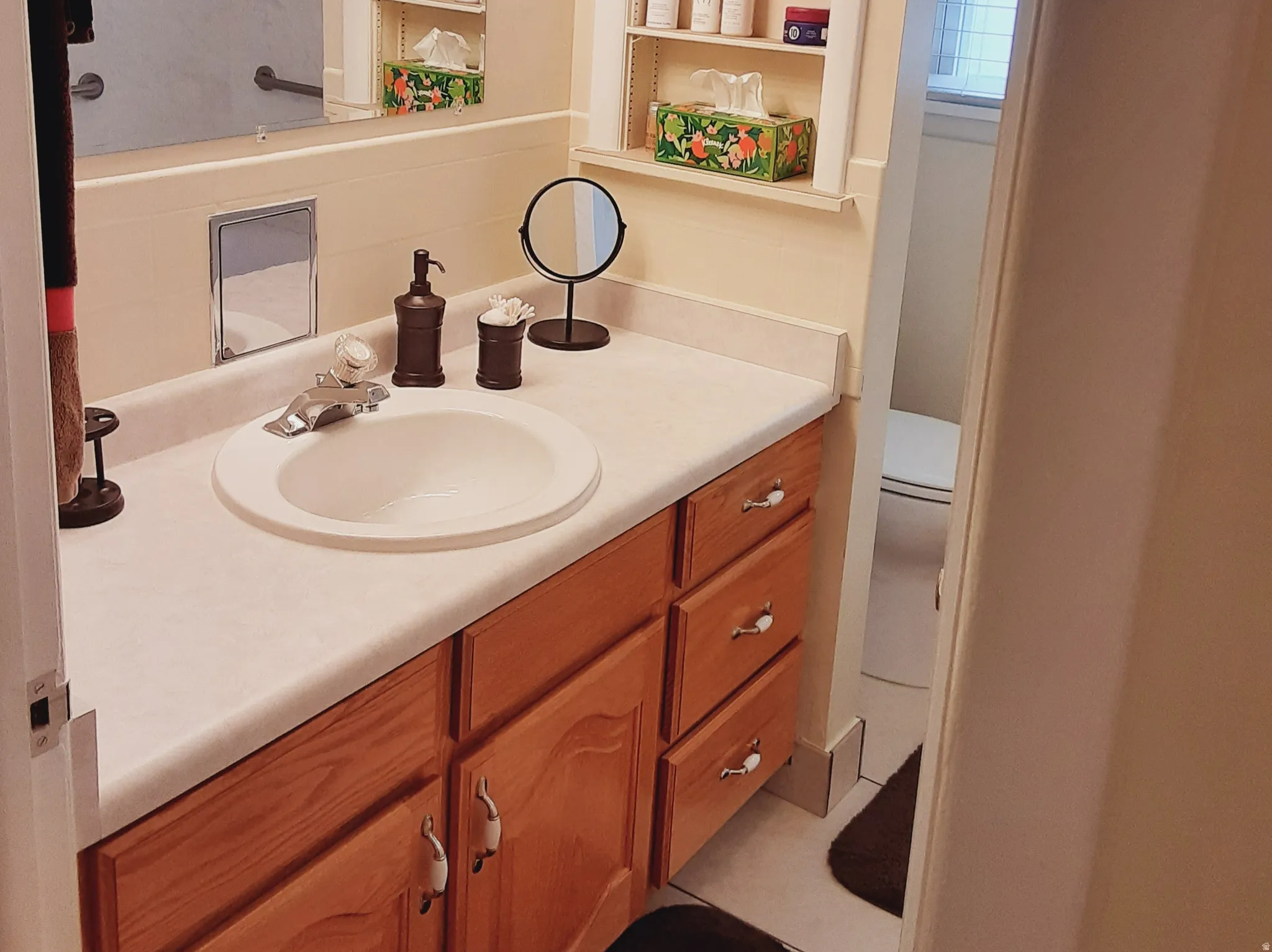 Wood-finish vanity with a single basin sink, light-toned countertop, and chrome fixtures