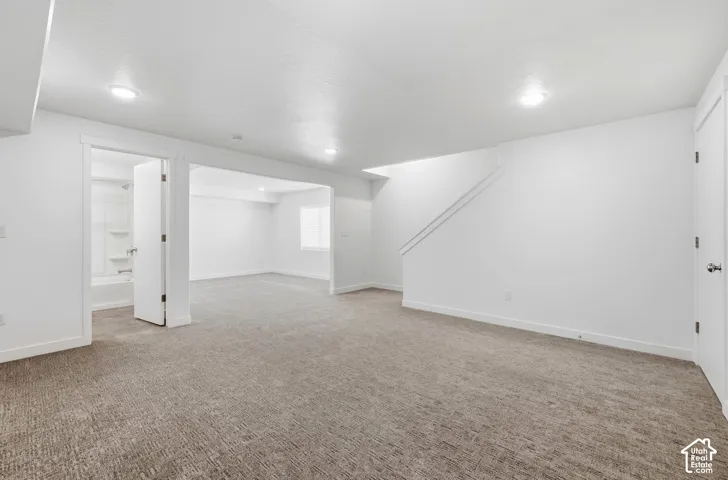 Spacious carpeted room featuring recessed lighting and a doorway to a bathroom with a white tub-shower combination