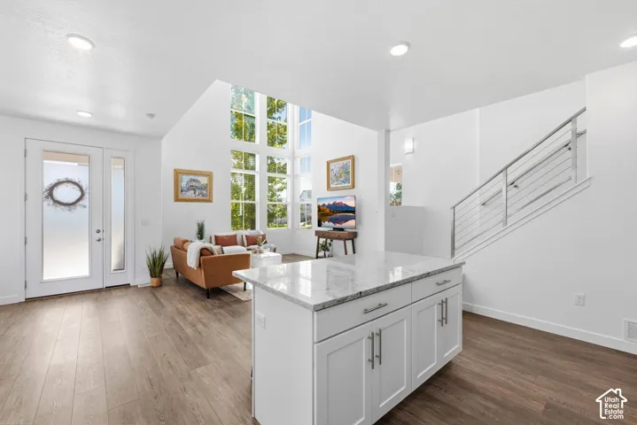 Kitchen island with granite countertop and white cabinetry, laminate flooring, two-story living area with expansive windows, and a staircase with a cable railing system