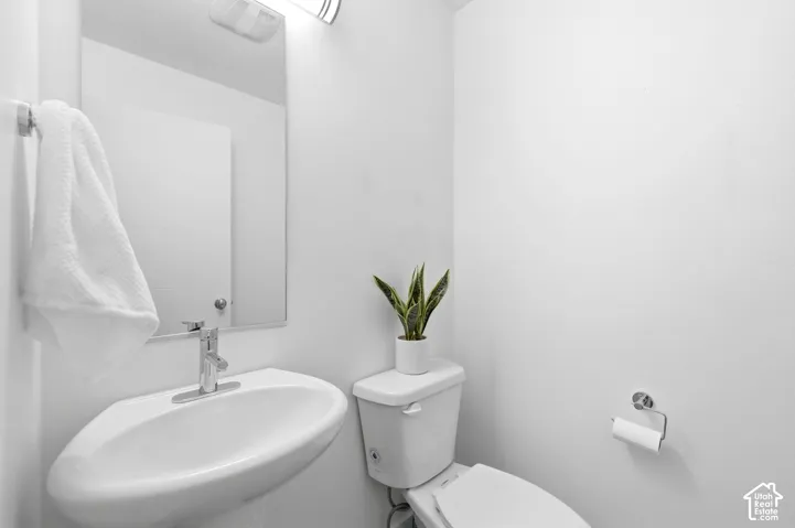 main floor half bath with pedastal sink with chrome faucet, complemented by a rectangular mirror and overhead lighting