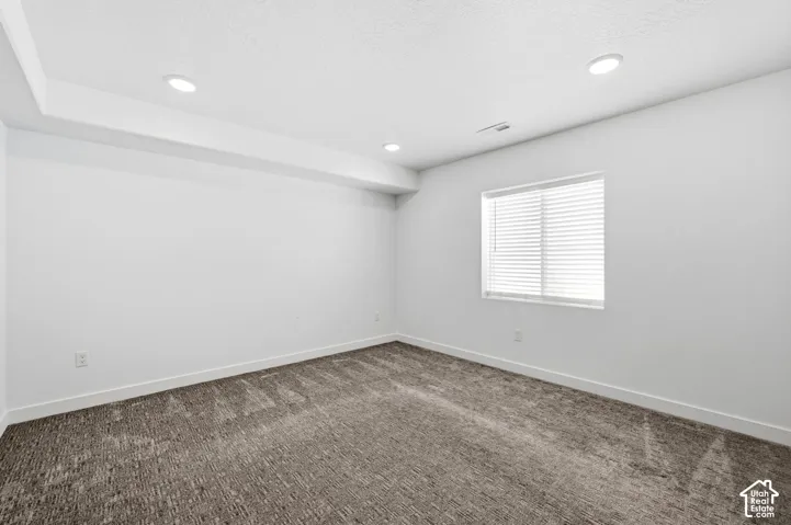 Recessed lighting illuminates the space, featuring white walls, a single window with blinds, and carpeting
