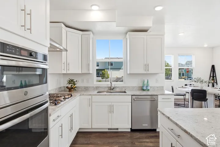 Kitchen featuring white shaker cabinetry, stainless steel appliances, light-toned granite countertops, a stainless steel sink, and laminate flooring